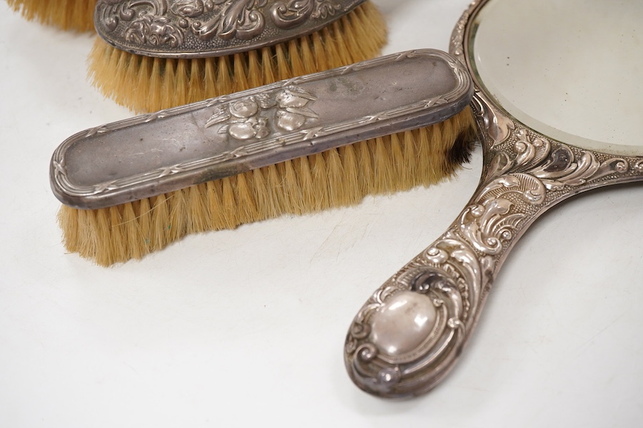 Four assorted early 20th century repousse silver mounted dressing table items to include a hand mirror, two hair brushes and a clothes brush(a.f.).